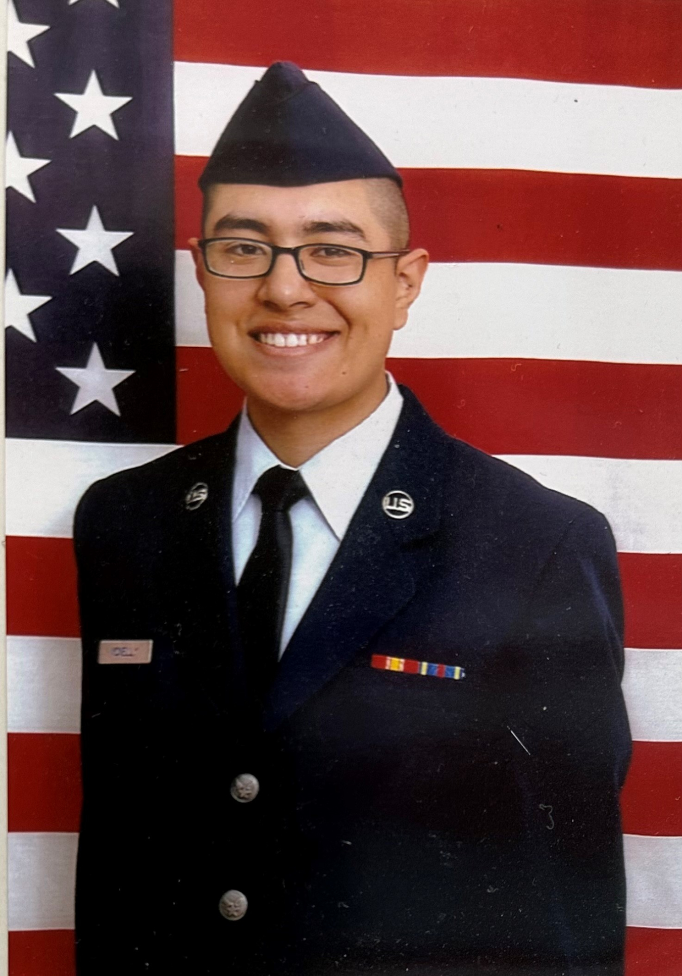 Man in uniform stands in front of American flag.