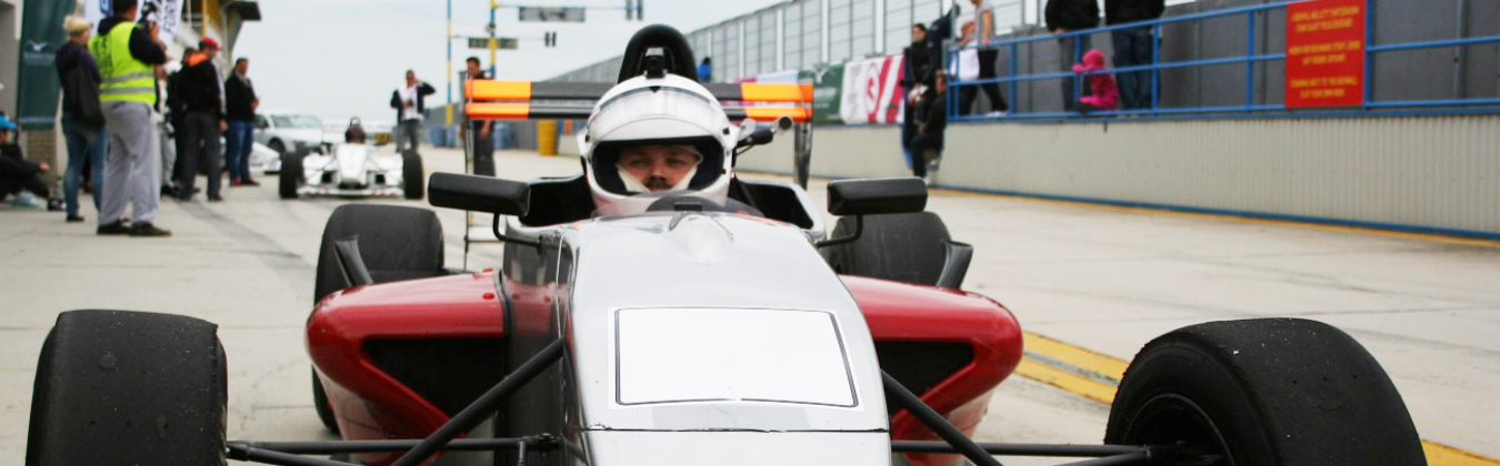 A person in a helmet drives a Formular racing car on a track. You can see the person's face.