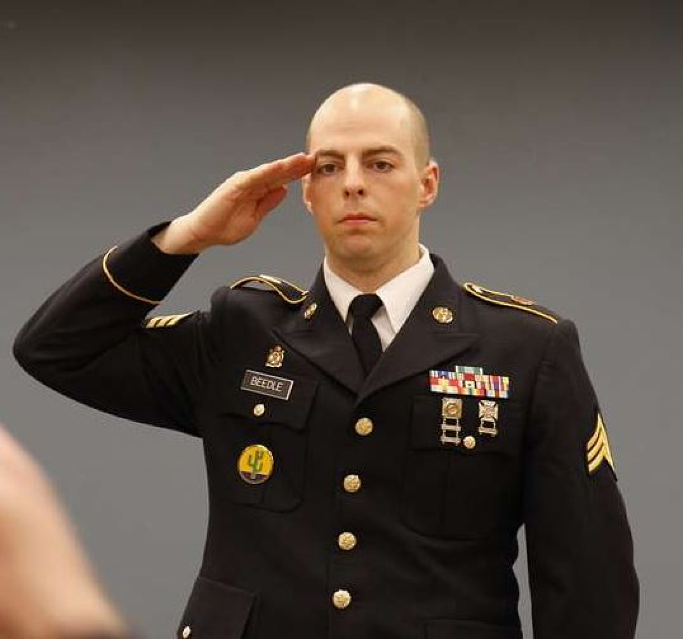A man stands in military uniform and salutes to someone standing behind the camera