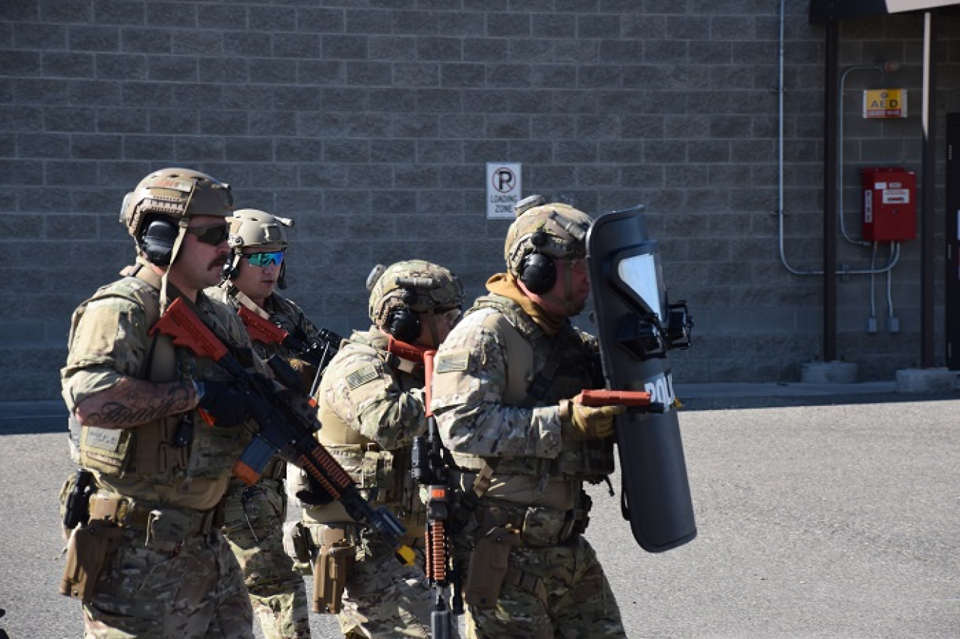 Four individuals dressed protective gear for an assailant drill, they hold fake guns and other tools