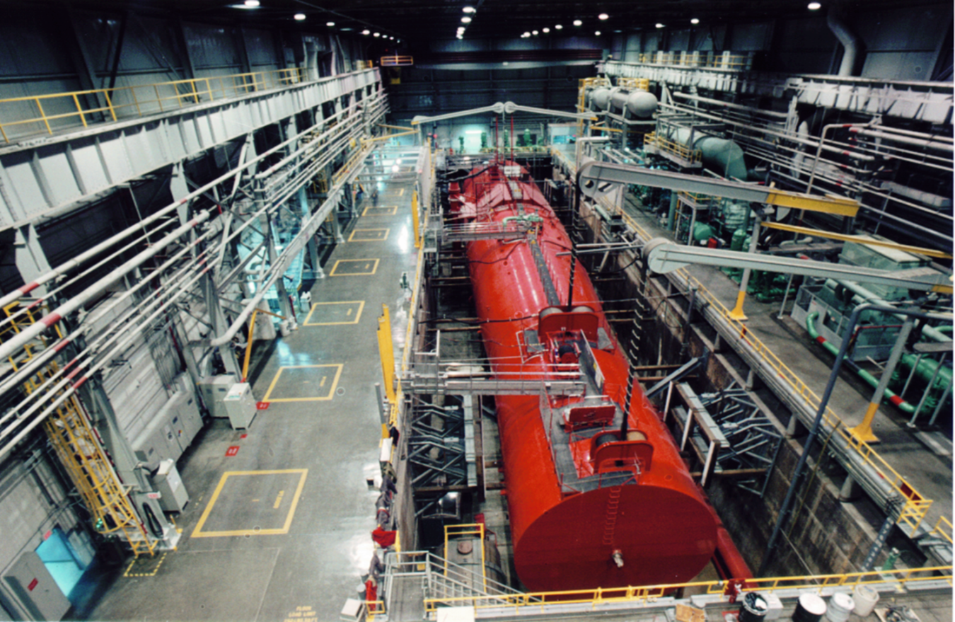 The inside of a large lab building that is storing a large red naval reactor