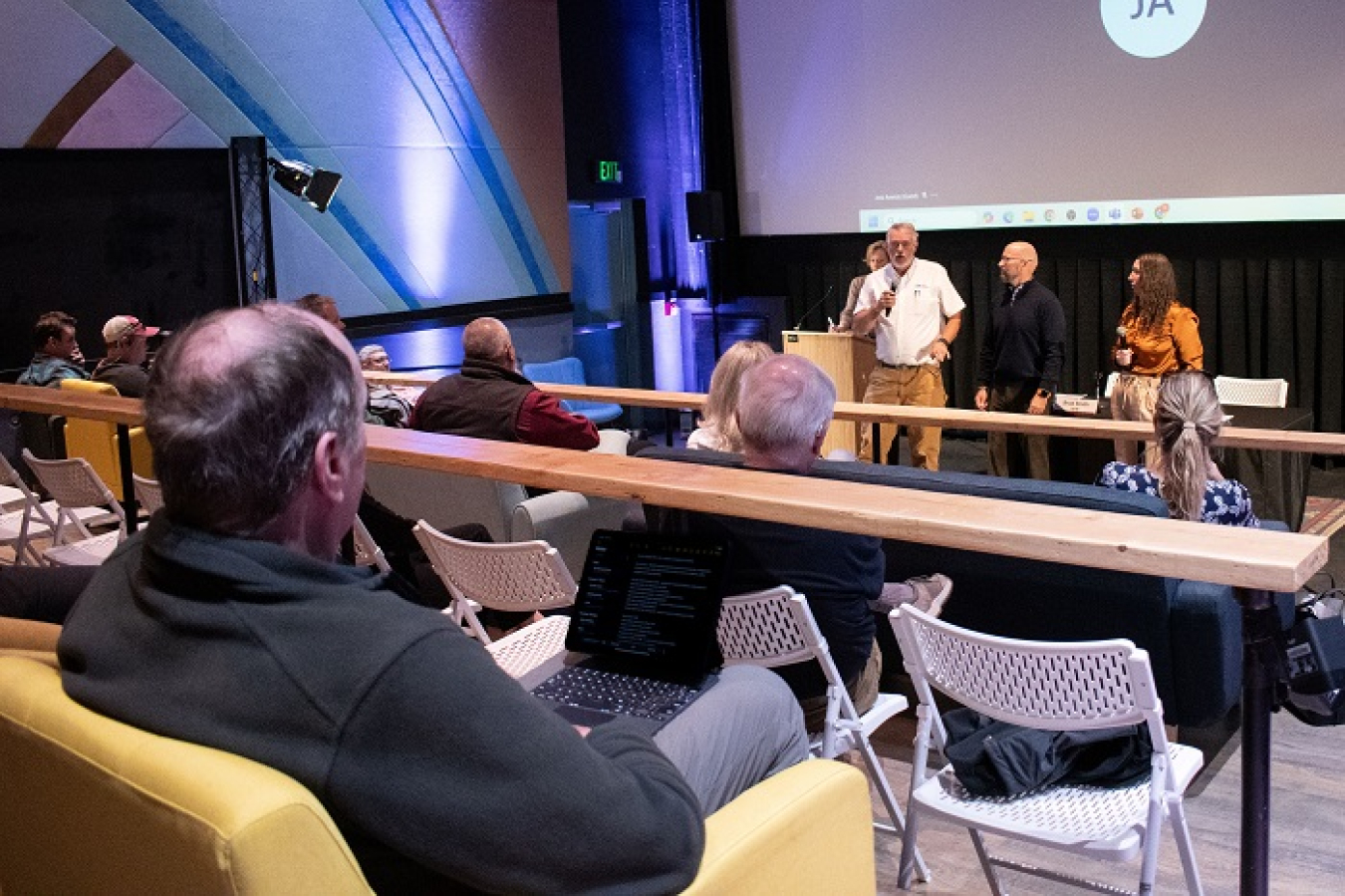 A panel of people stands at the front of a room and addresses an audience