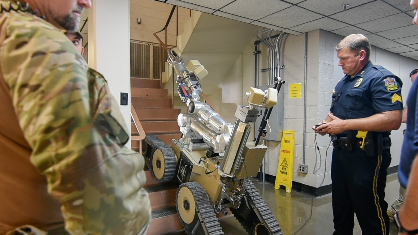 A person stands next to a bomb squad robot located on a staircase.