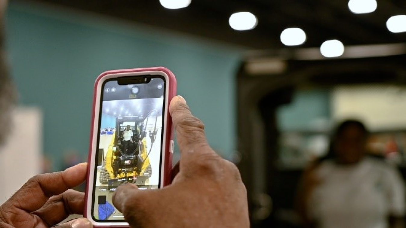 An upclose shot of someone holding an iPhone with the camera open taking a picture of a person sitting in a work vehicle