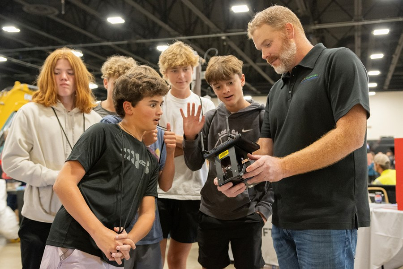 A group of students stand around an iPad held by a professional and they look at the screen