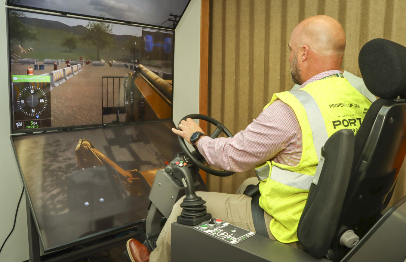 A man sits in front of monitors in a chair that mimics being inside a machine vehicle, he is facing the screen