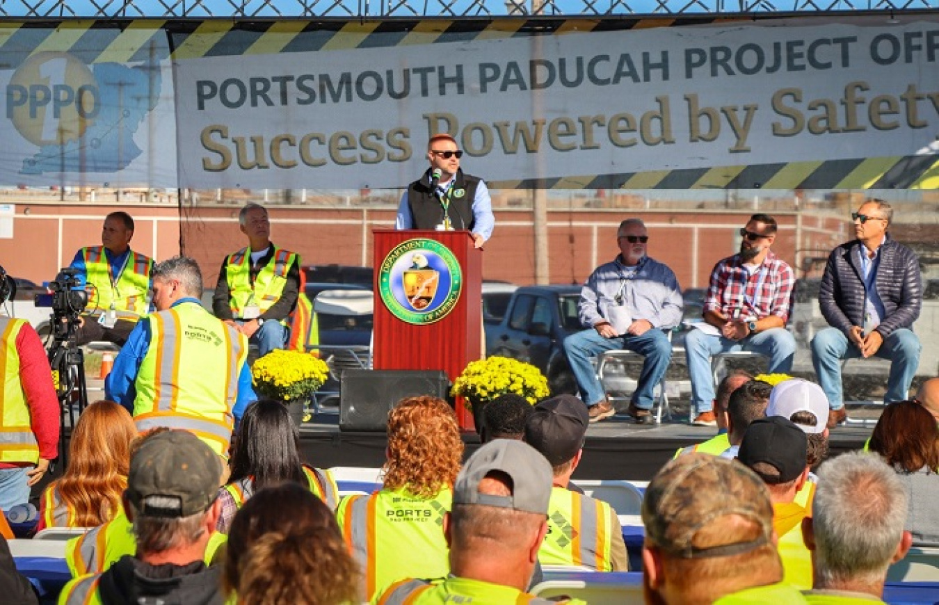 A man stands behind a podium on a stage and addresses an audience
