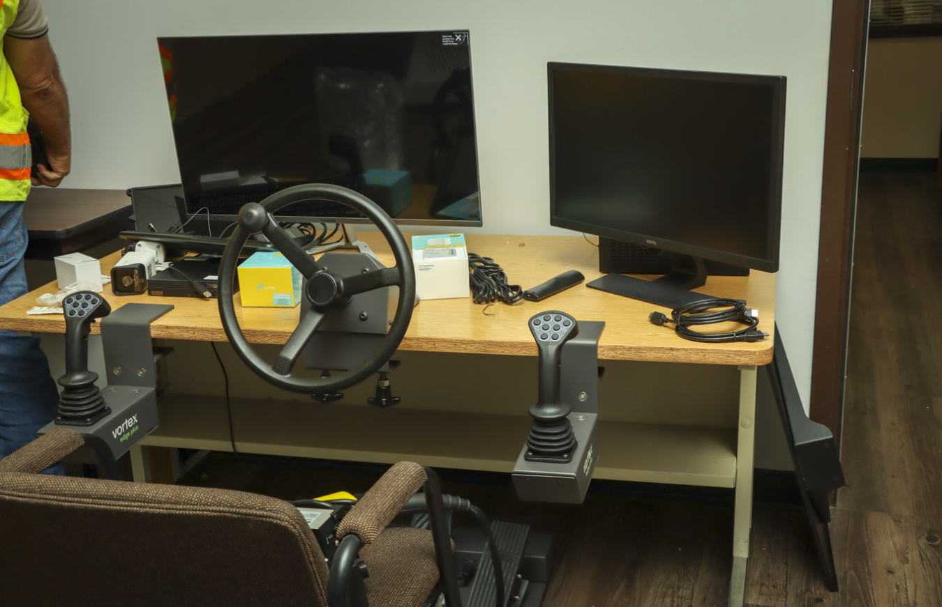 A table with two monitors on top of it and a steering wheel and pedals attached to it, a chair is in front of the desk