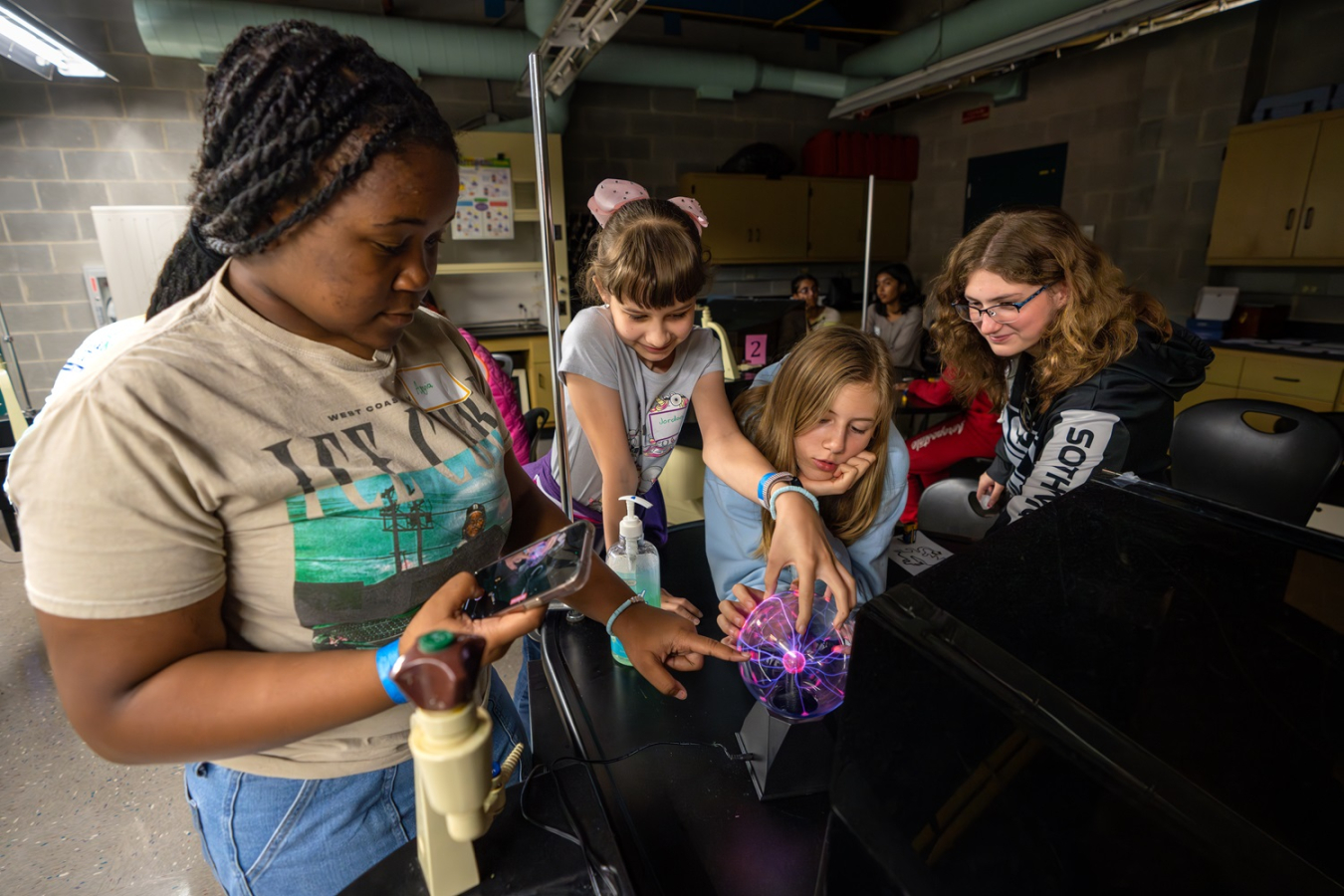A group of middle school girls look at an object on a table during a STEM activity