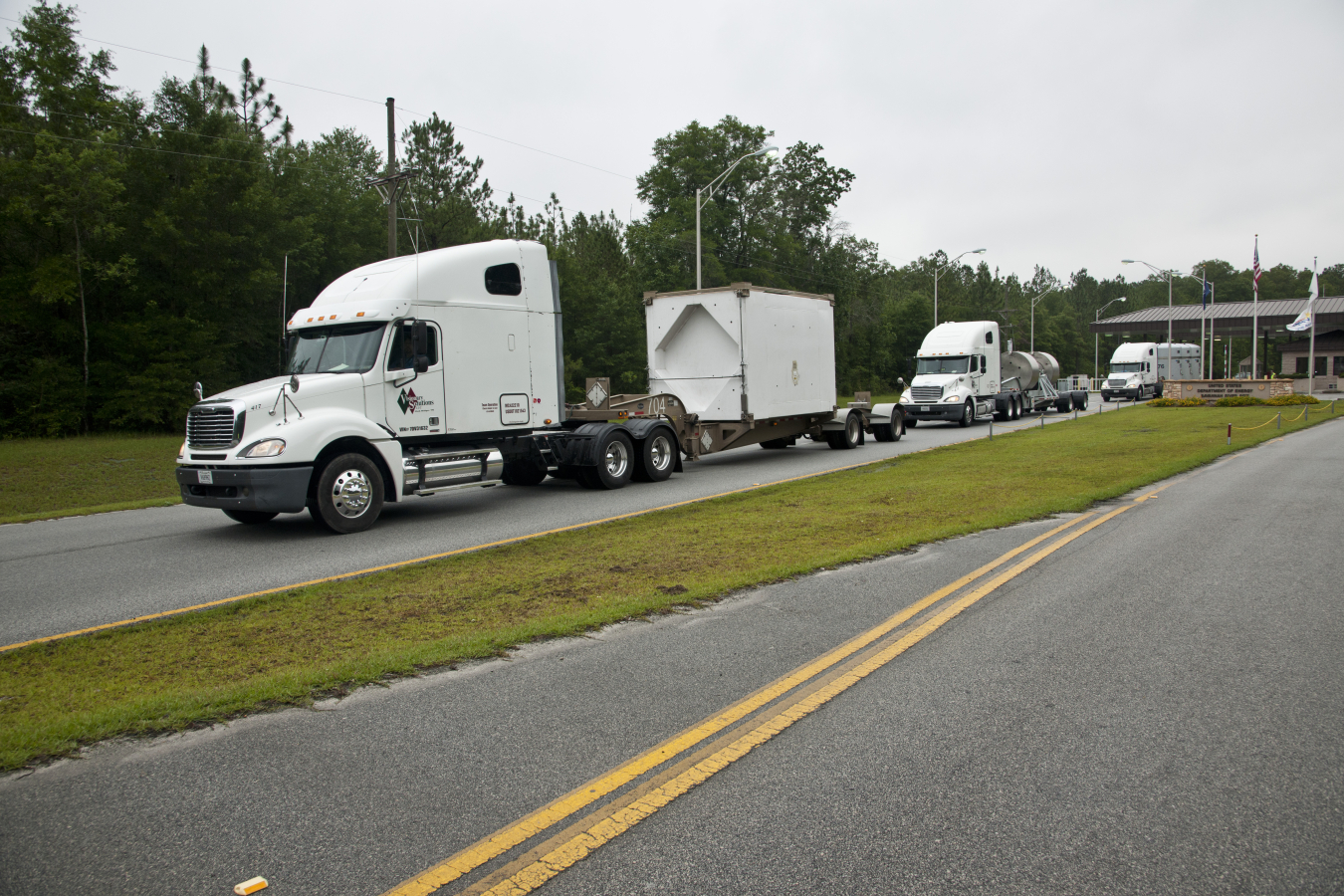 Three white trucks with waste boxes on the back, driving on a road