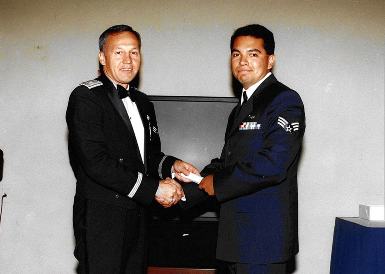 A photo of two men in military uniforms shaking hands and looking at the camera