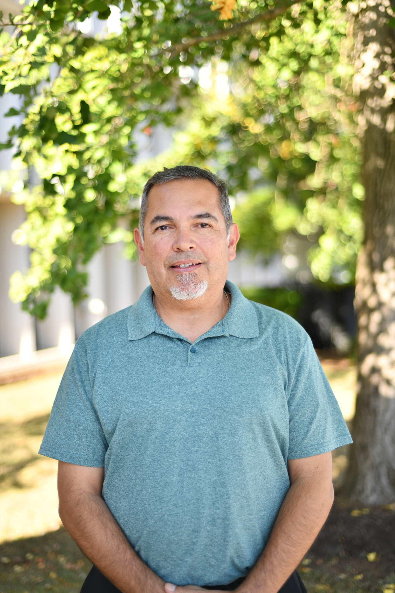 A headshot of a man in a blue shirt smiling while standing outside