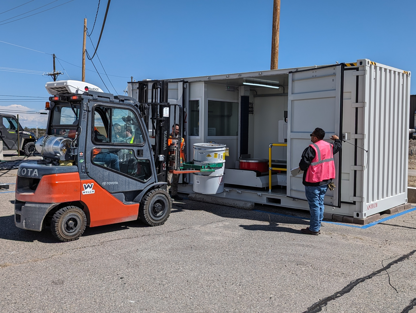 Front loader inserting waste container into small building.
