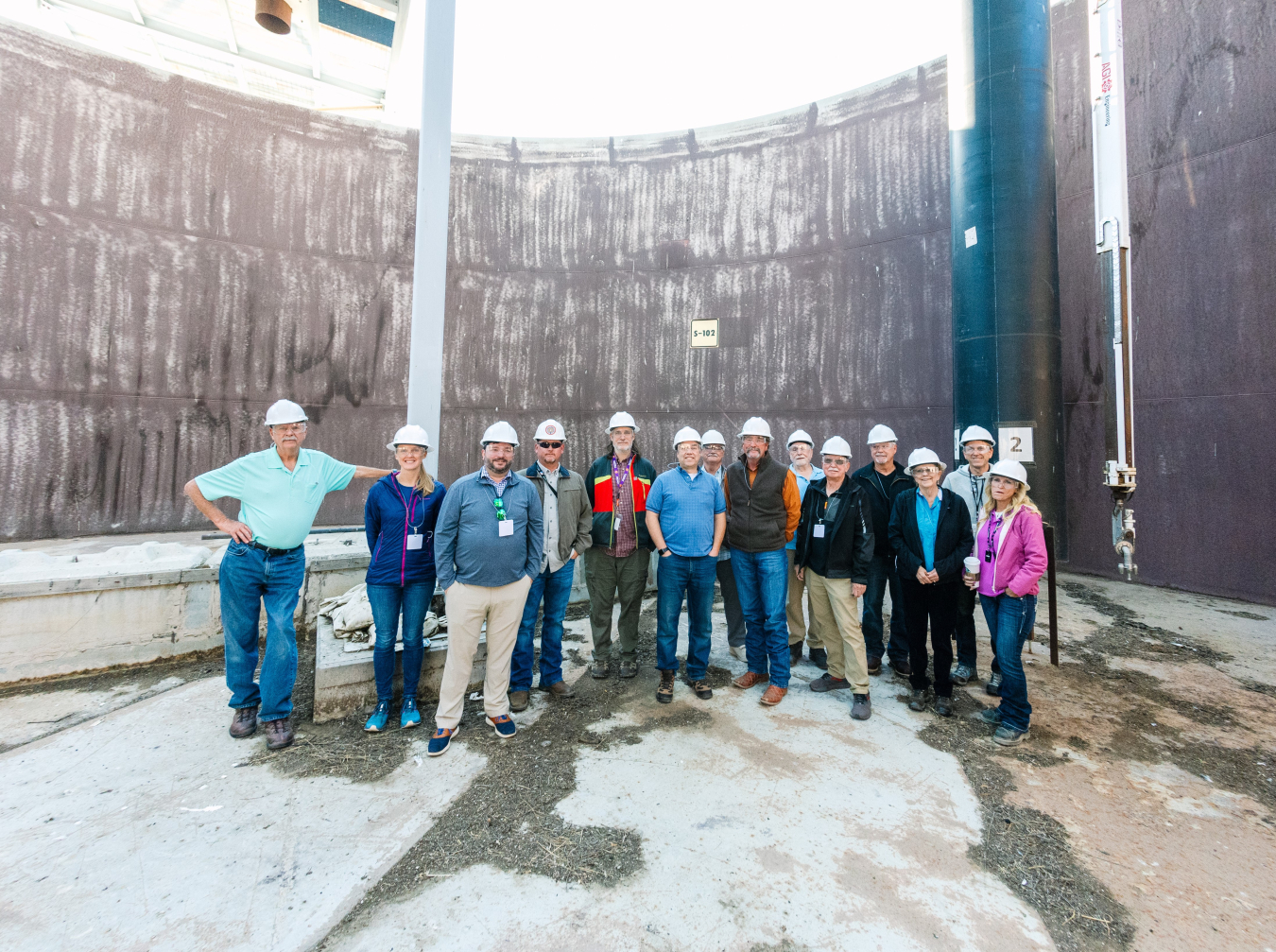 A group of people in white safety hats smile for a group photo