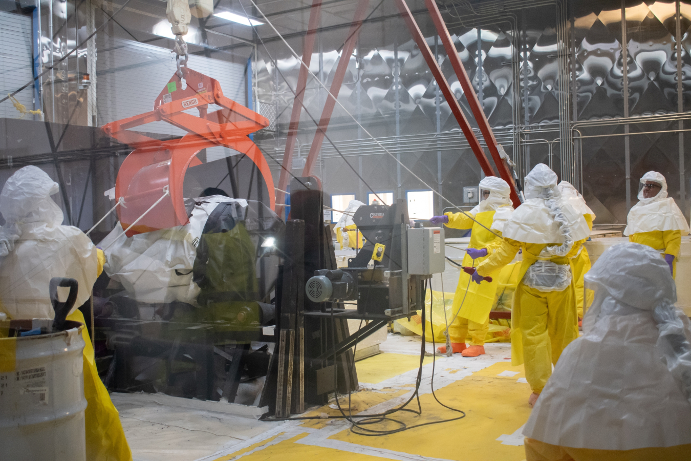 Workers in yellow hazmat suits use a pulley to lift up a machine