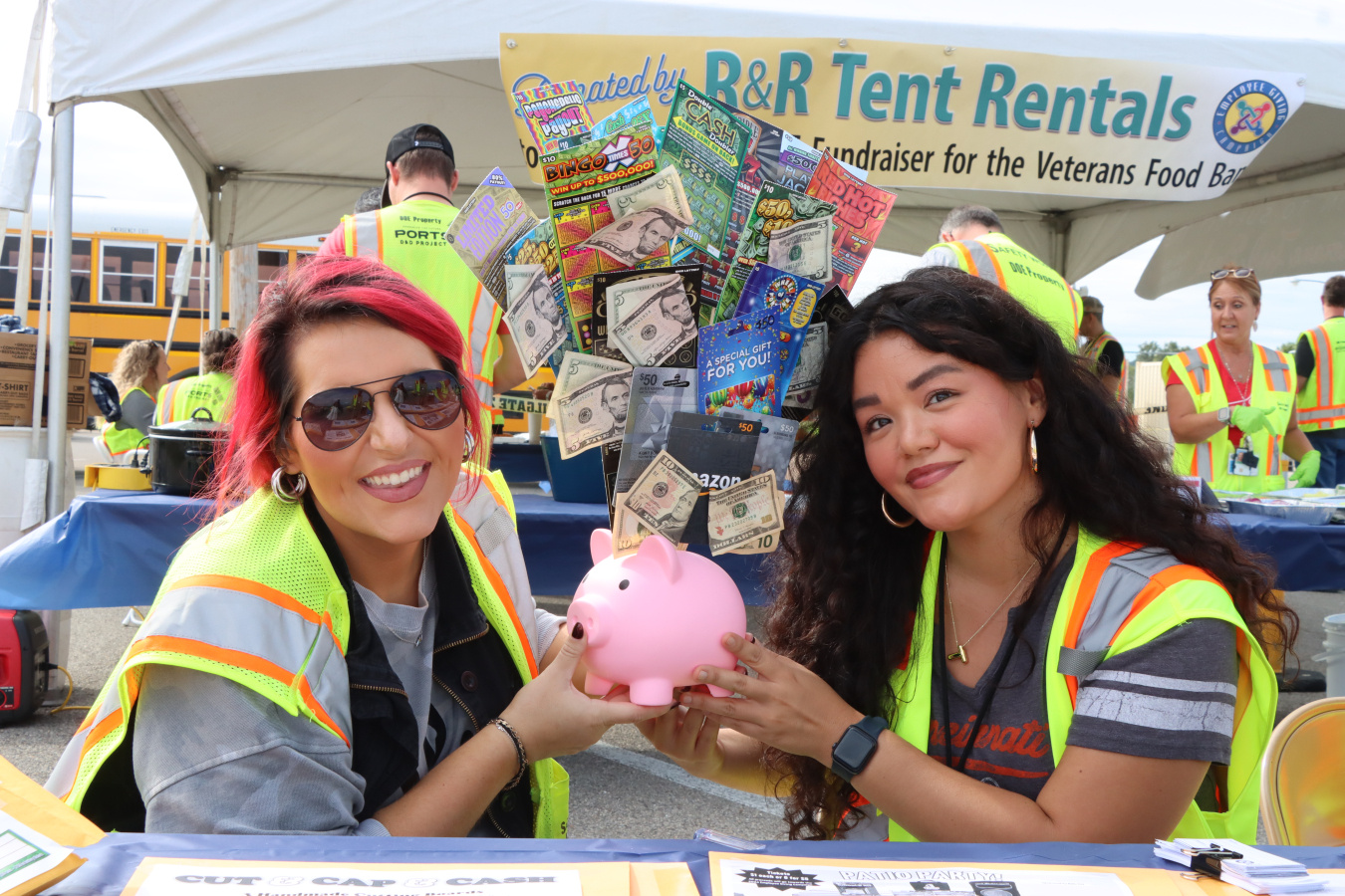 Two women smile for a picture while holding up a pink piggy bank