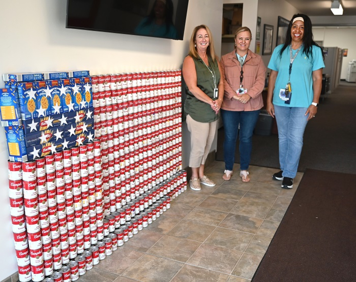 Canned and boxed food stacked to create an American flag with three woman posing for a picture beside it