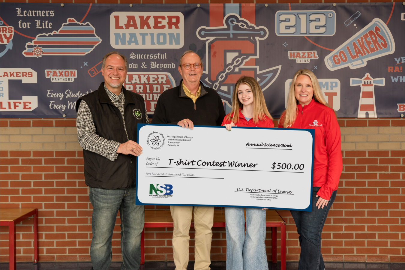 Four people pose for a picture while holding a large check for $500