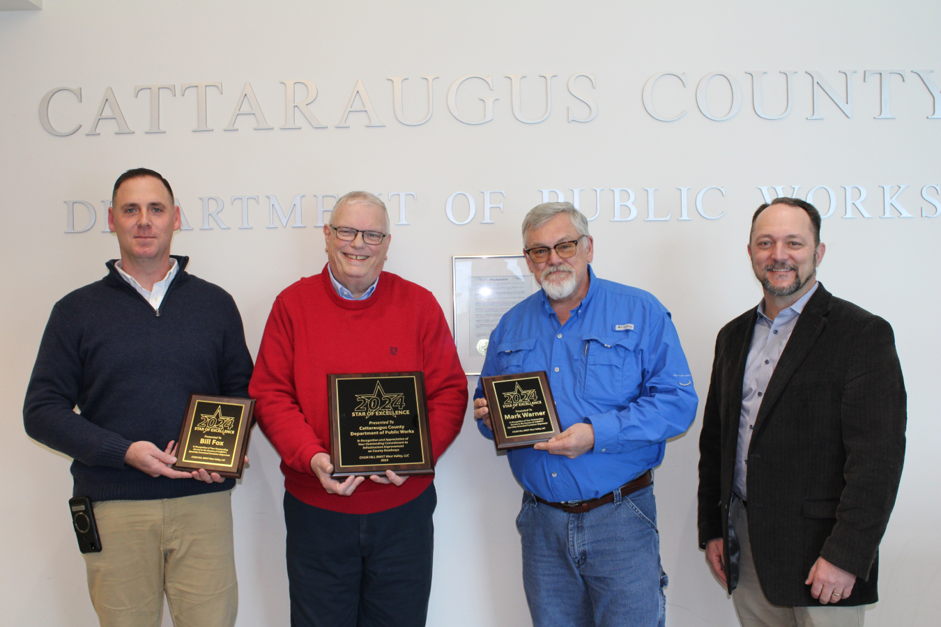 Four men pose for a picture, some of them holding award plaques 