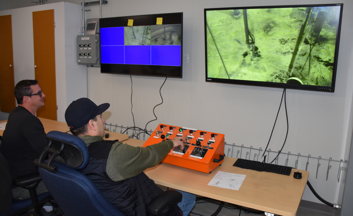 Two employees sit at a control desk and monitor screens