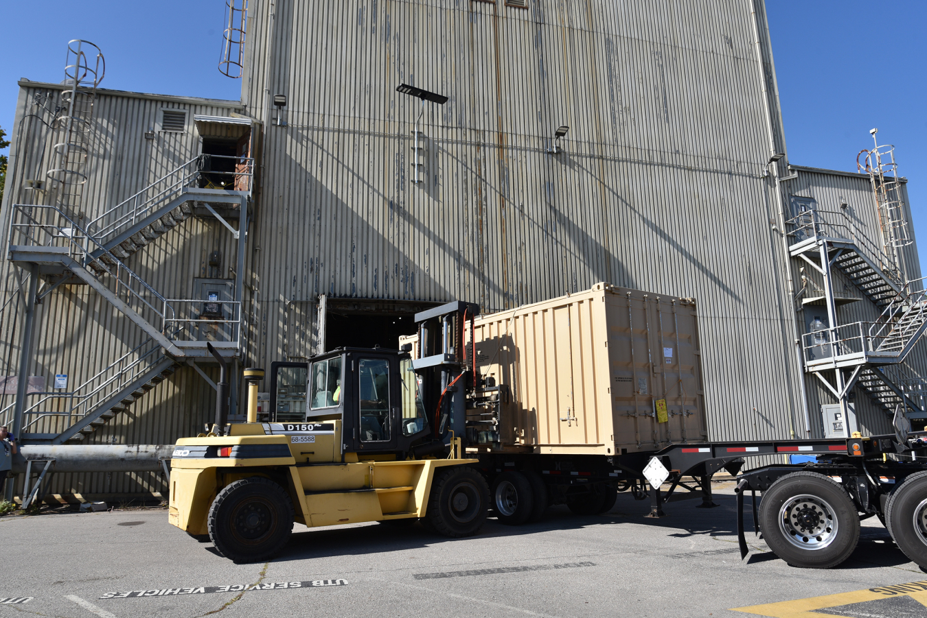 A yellow work vehicle in front of a large facility building