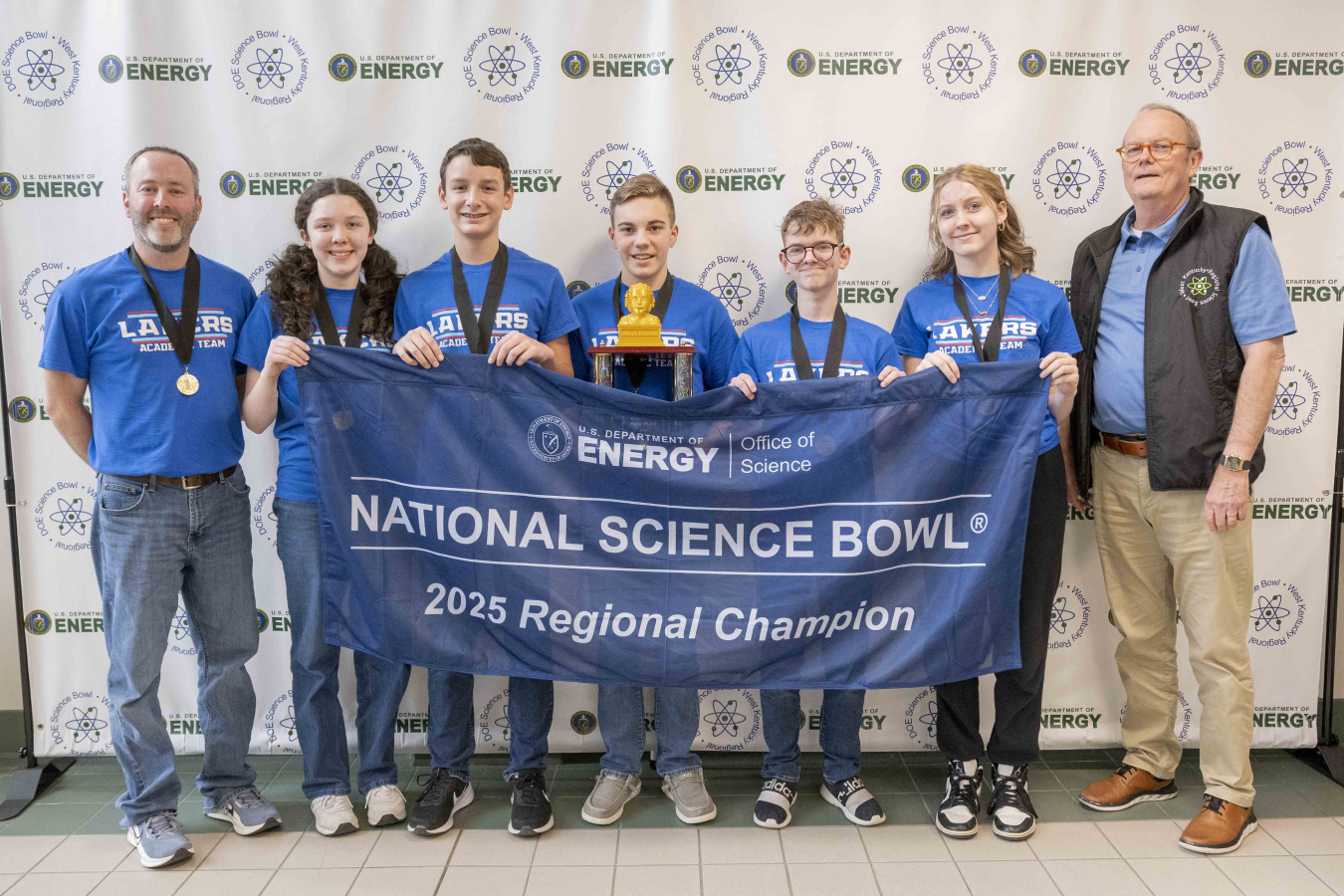 A group of midde school students holding a banner and trophy's after winning a science bowl competition
