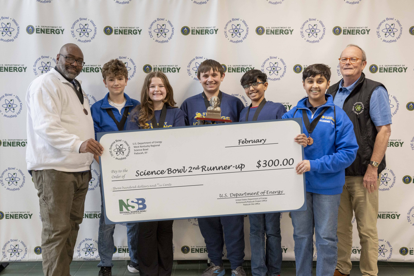 A group of midde school students holding a banner and trophy's after winning a science bowl competition