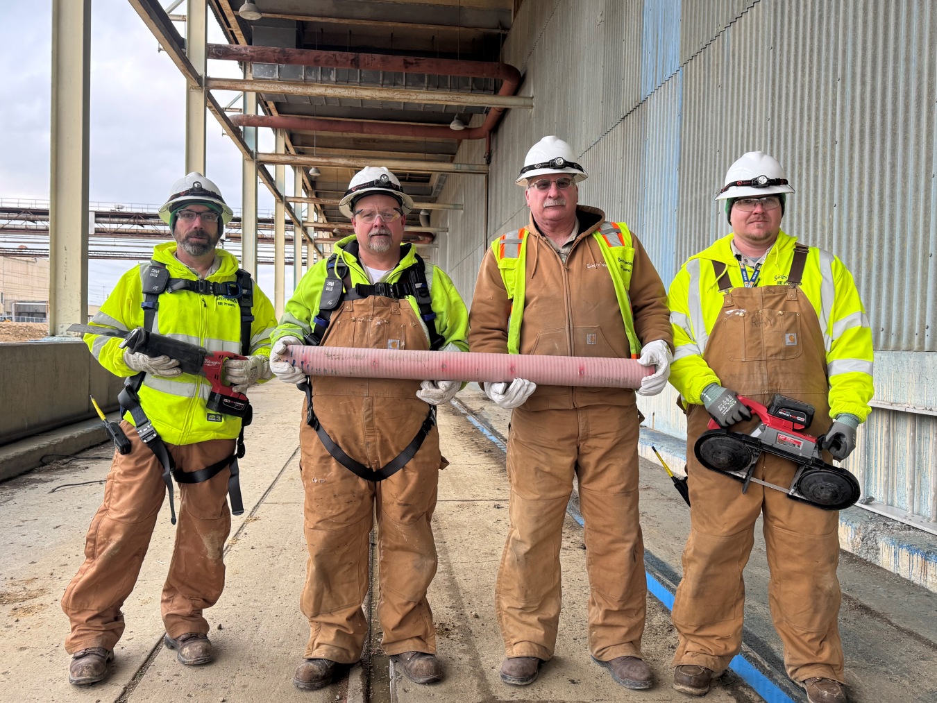 A group of employees hold a pipe and tools while posing for a picture