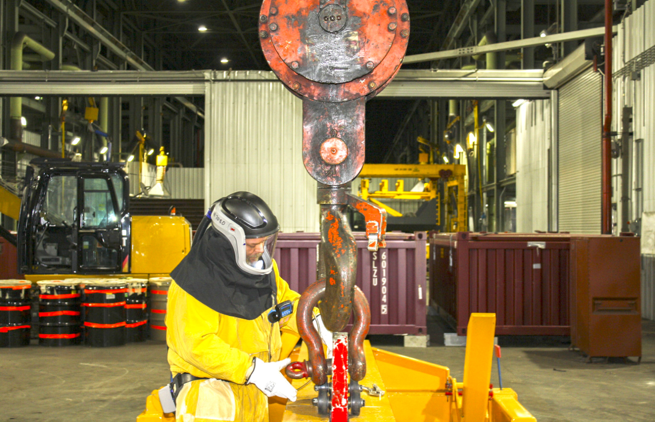 Employee in a yellow hazmat suits works on a lifting fixture