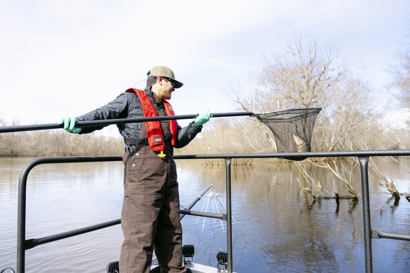 A man in a lifejacket standing with a fishing net that has a fish in it