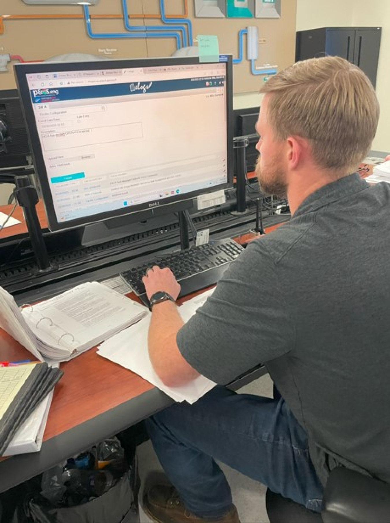 An employee sitting at a desk working on a computer with papers and binders on the desk