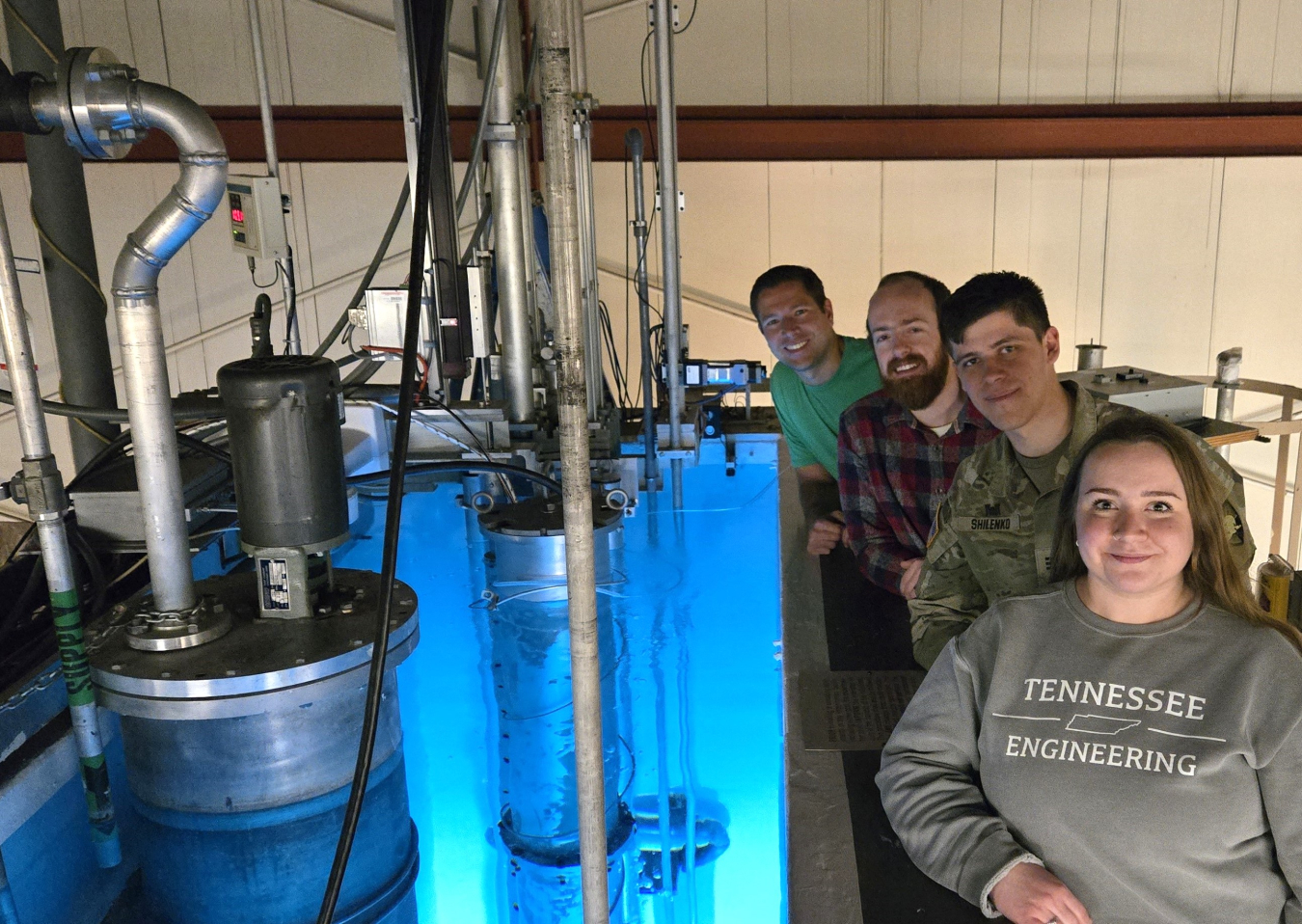 Four people stand to the right of a university reactor