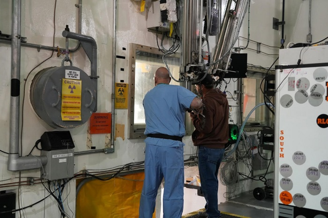 Employees at the Transuranic Waste Processing Center stand with equipment at glass to process the radium-226 boron source to prepare it for shipment and disposal.