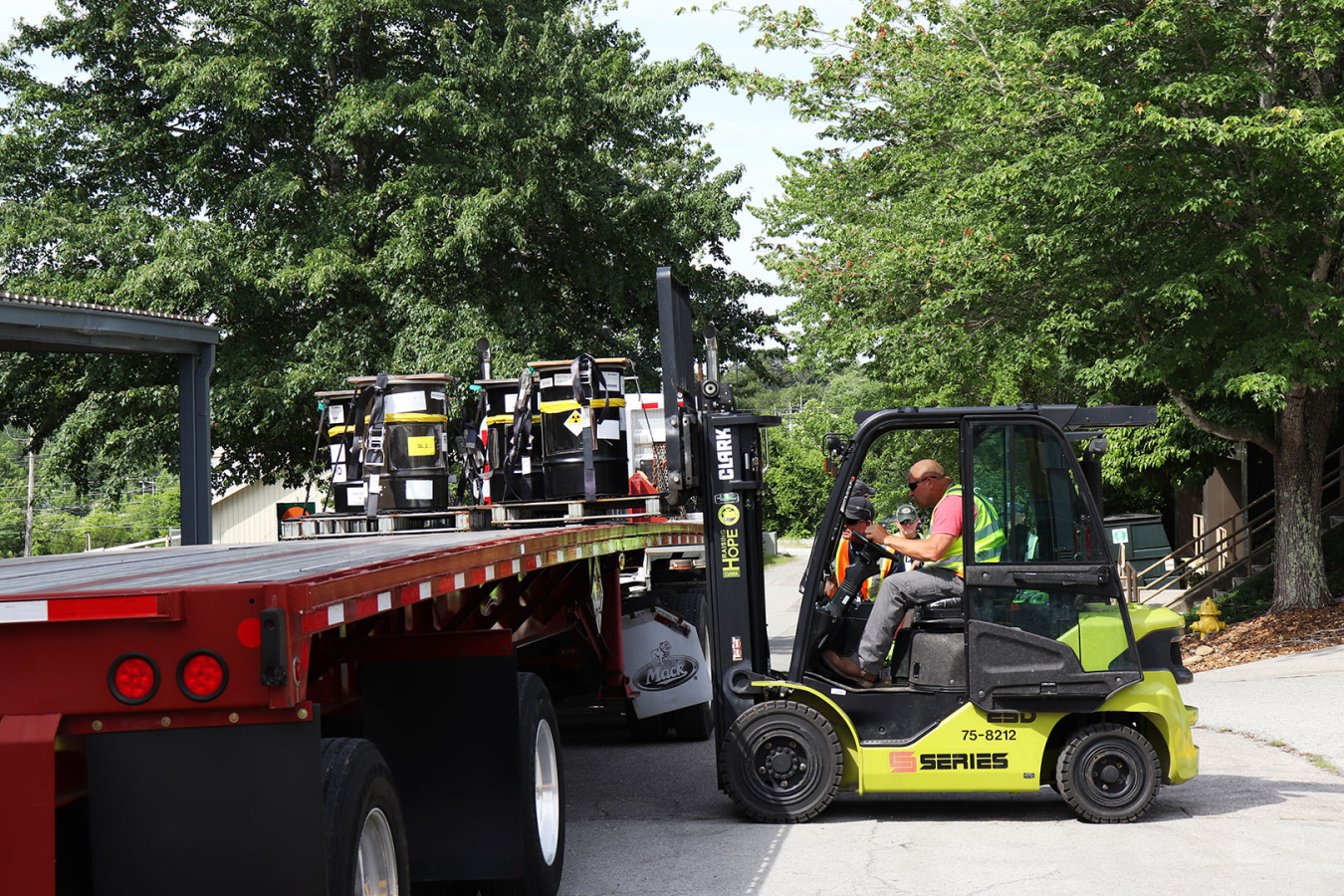 A smaller work vehicle loading storage drums onto a large truck