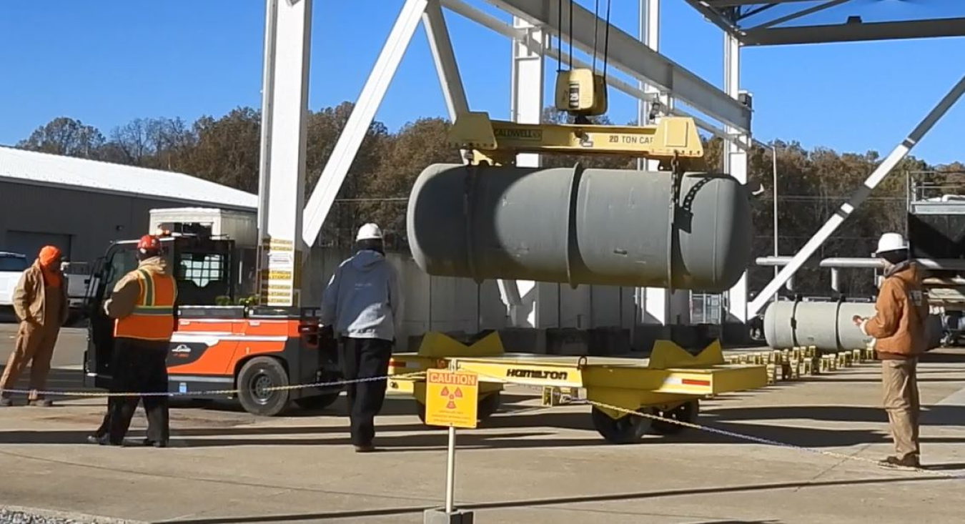 Employees using a tow motor to move a cylinder
