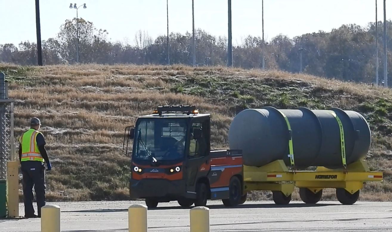 Tow motor and cart carrying a cylinder as it drives around the site