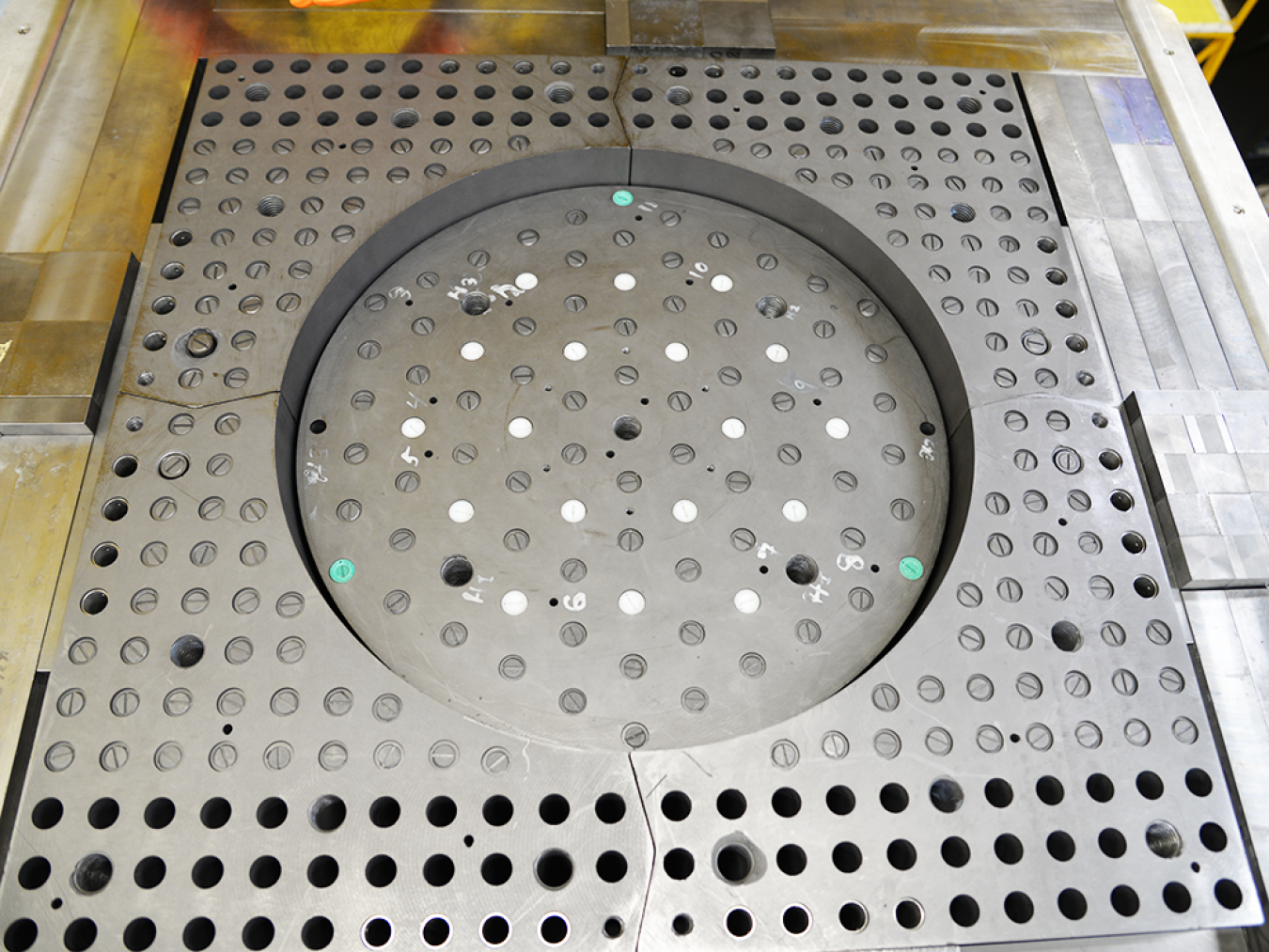 THETA experiment core, a metallic square perforated by numerous holes with a circular depression in the center.
