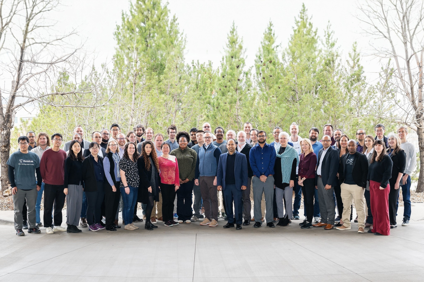 A large group of people stand together outside in front of trees during kickoff week.
