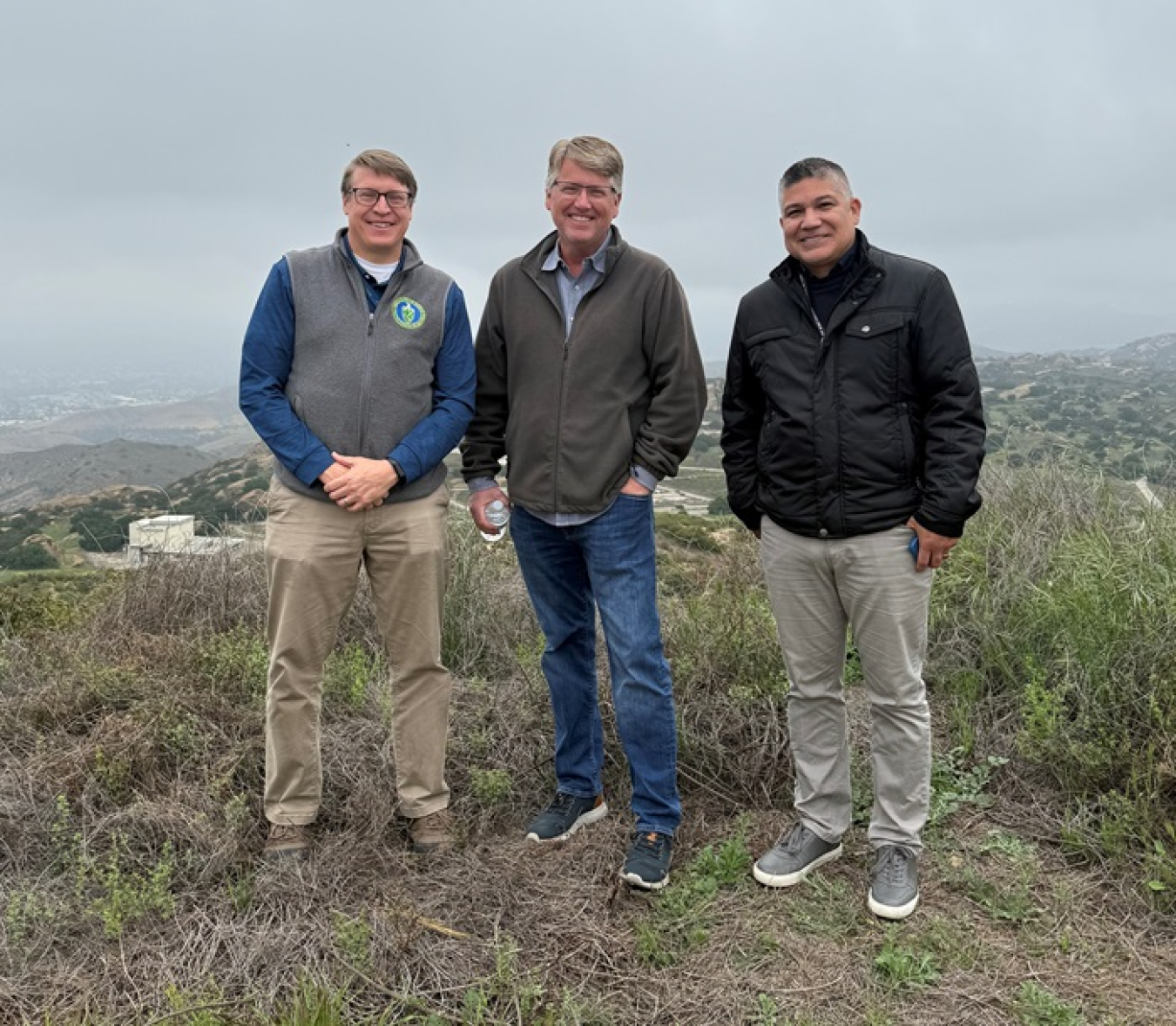 Three men stand outside in front of foggy mountains and valleys