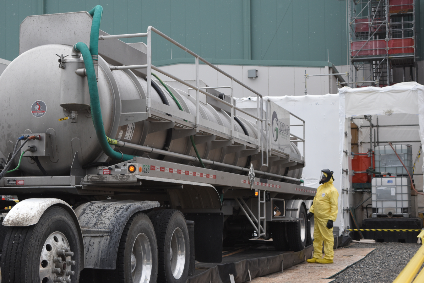 A large tank truck parked with an employee in a hazmat suit standing beside it