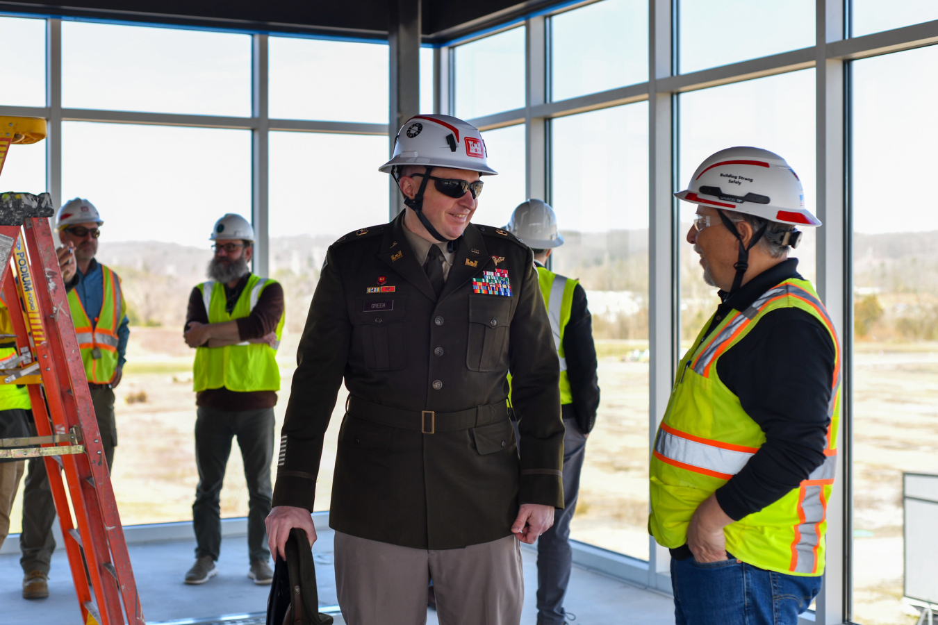 Men in protective gear stand inside a room with lots of windows