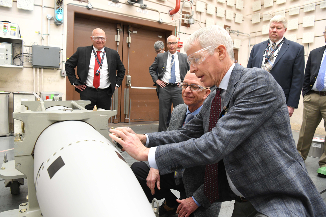 Secretary of Energy Chris Wright holds a stamp above a B61-13 with men in suits looking on in the background