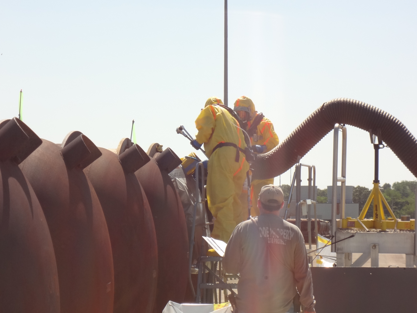 Employees in safety gear replace valves on large metal cylinders