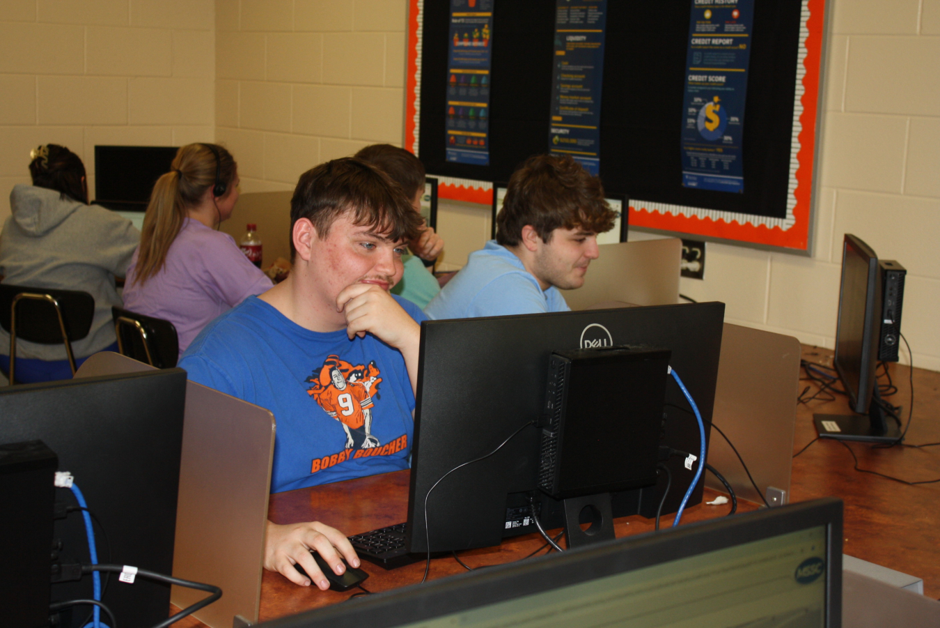 Students sit in a computer lab and work at the computers
