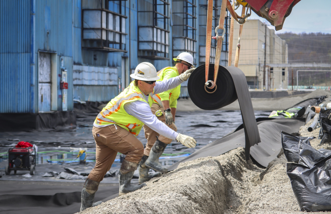 Employees rolling out a line of black liner outside a building