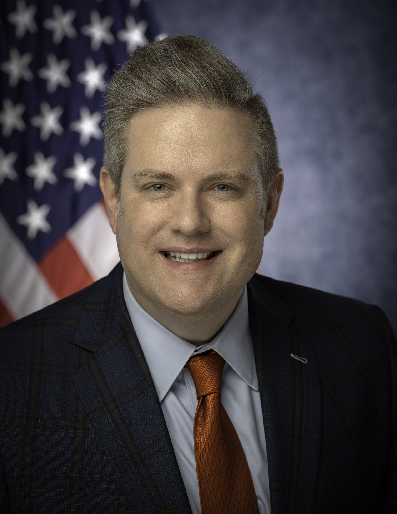 headshot of Charles Moran in a suit and tie with American flag in background