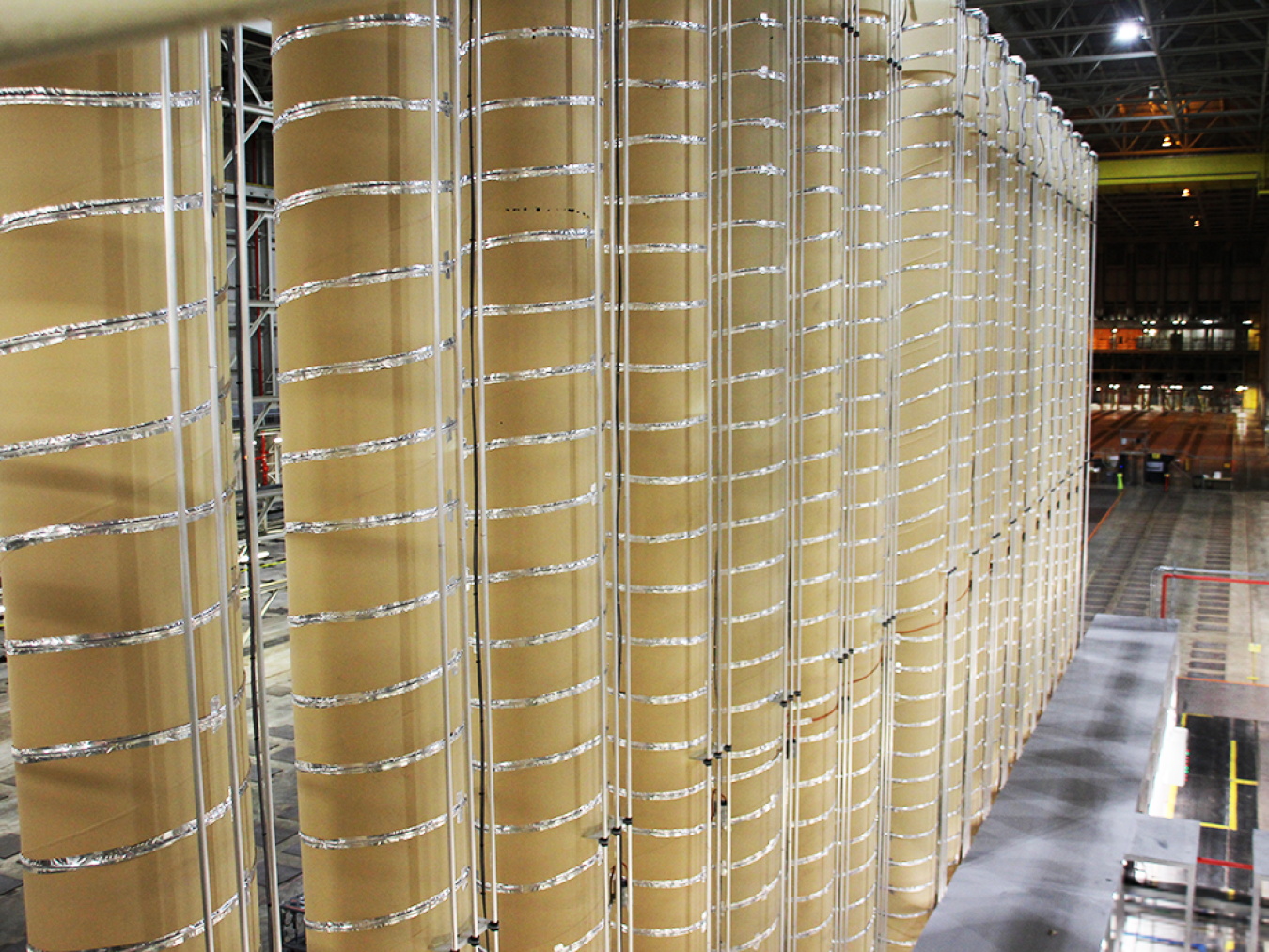 Tall, narrow tan-colored cylinders with coiled metal wire around them form a HALEU enrichment cascade.