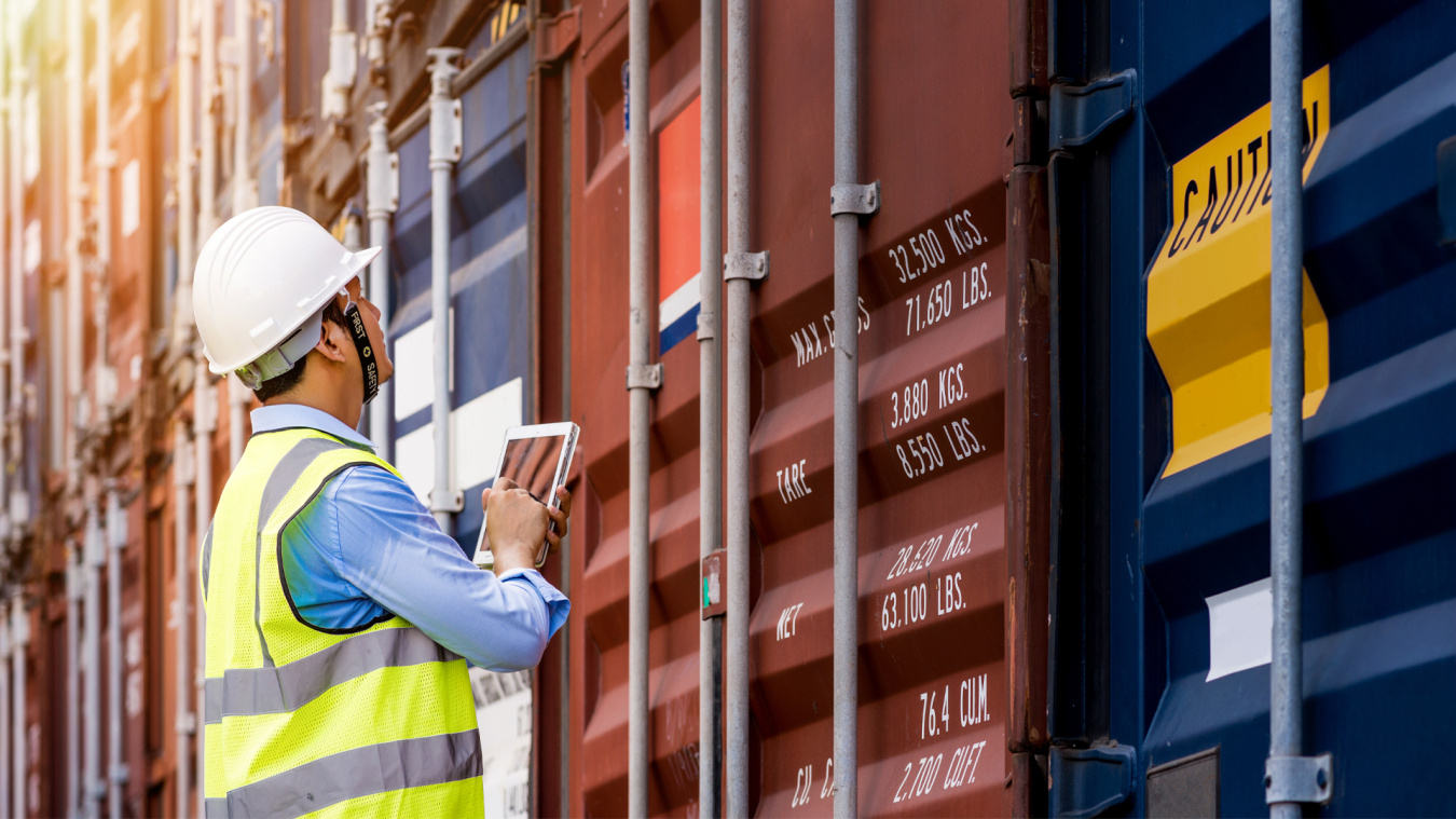 A man in a hard hat looks at shipping containers