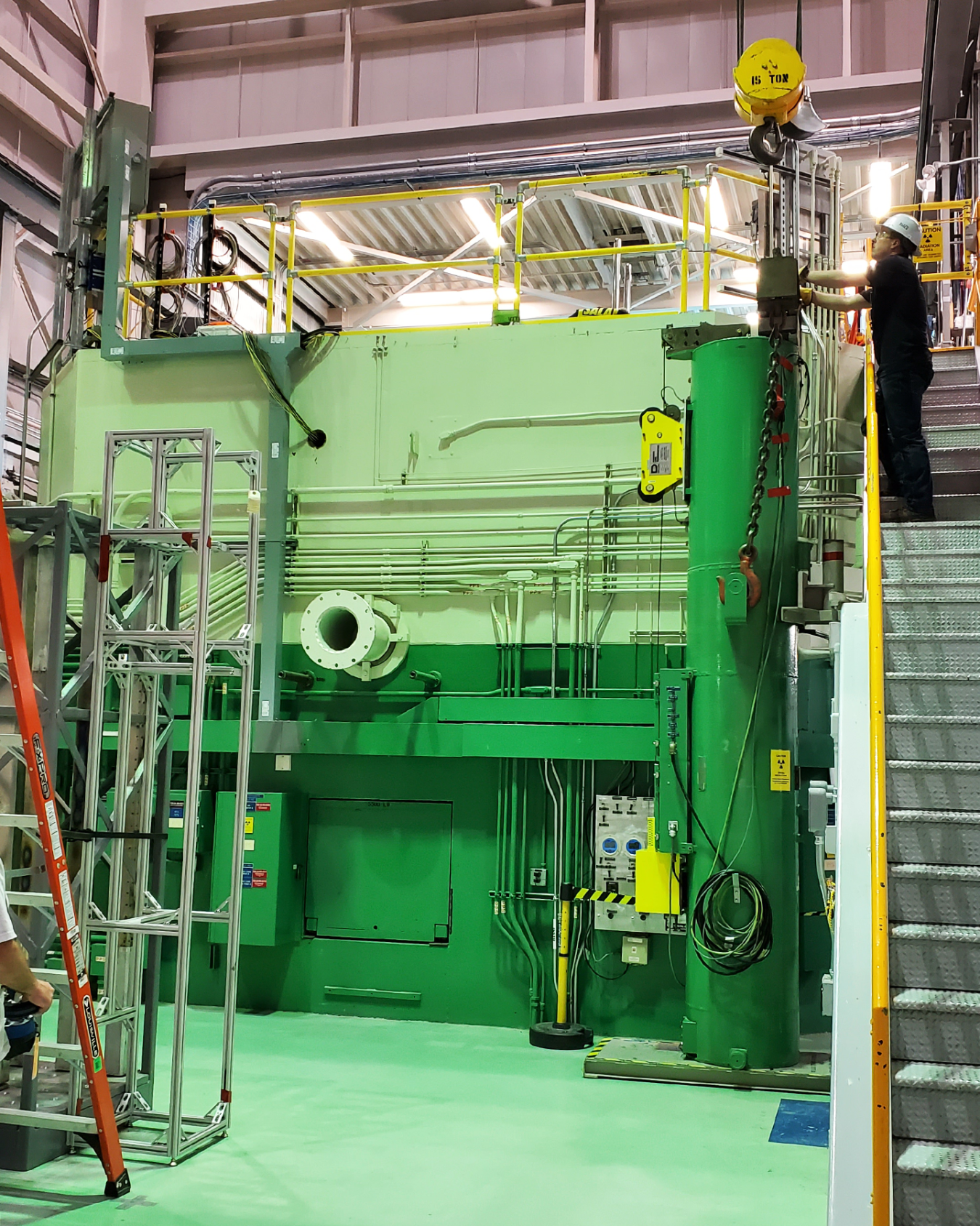 A worker stands on a staircase next to INL's TREAT reactor, a large square piece of scientific equipment painted green.