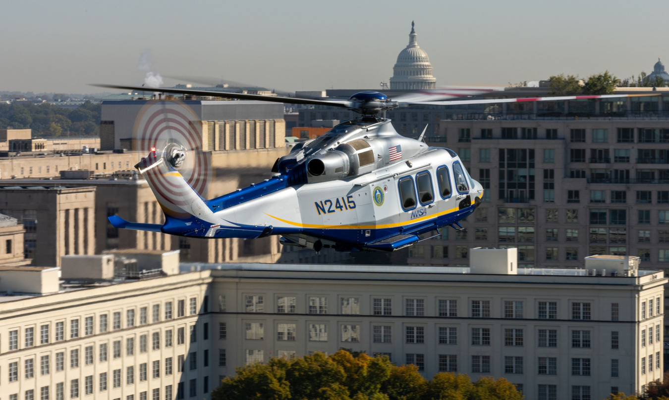 A photo of an NNSA helicopter flying over buildings. The U.S. Capitol is in the background